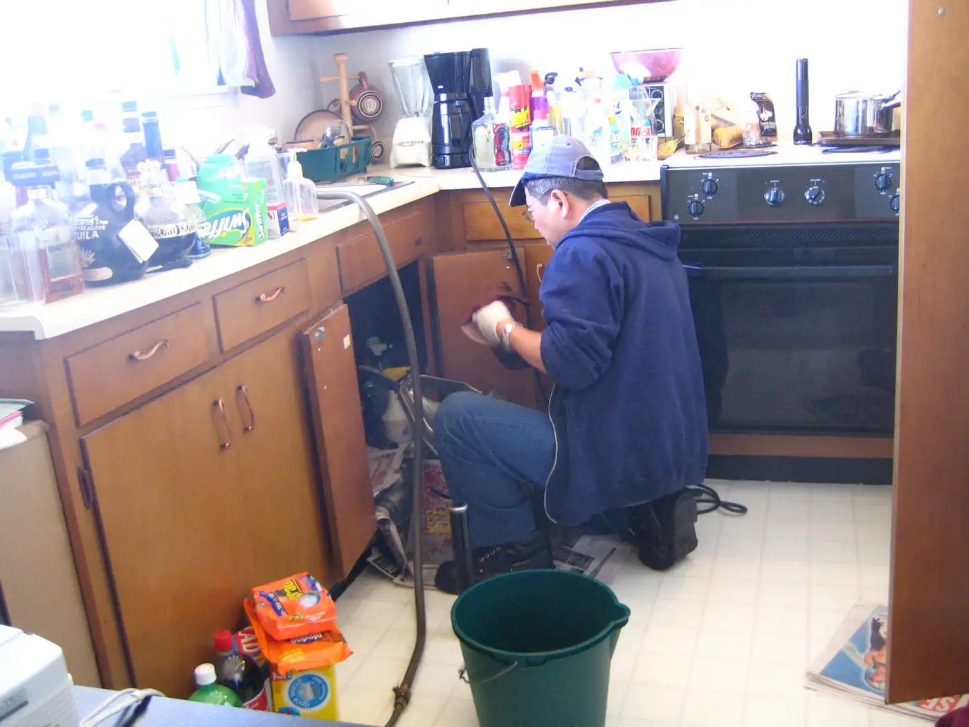 A plumber kneeling at a kitchen sink cabinet